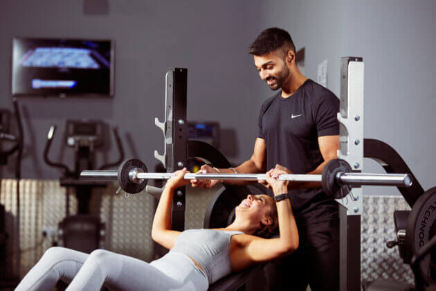 Photo of a woman lifting weights with a trainer assisting