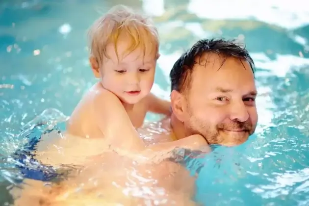 man with young child in swimming pool