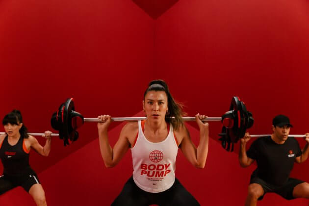 three adults supporting weights bar across their shoulders